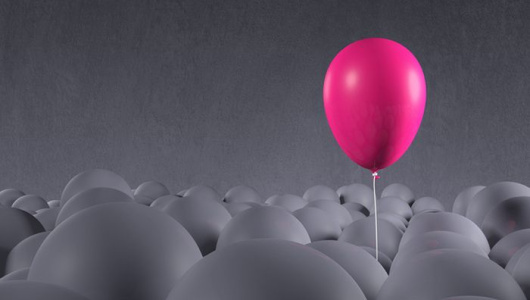 Bright purple pink party balloon emerging from a crowd of dark, gray anonymous balloons. Being special, standing out from the crowd, focusing on own individuality. Front view, looking up. Copy space on dark side of image, gray background.