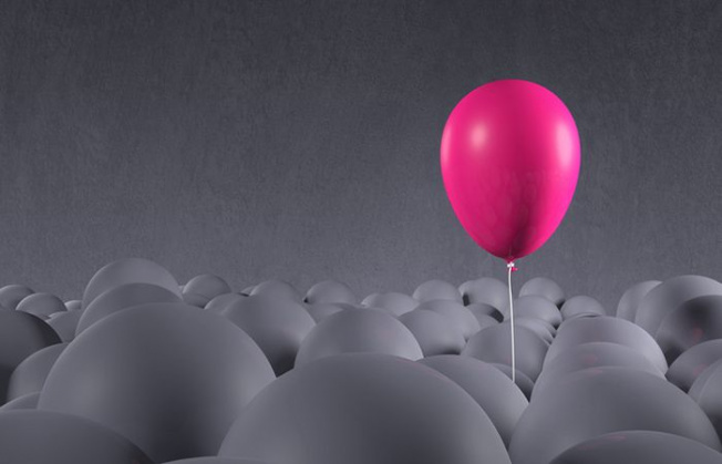 Bright purple pink party balloon emerging from a crowd of dark, gray anonymous balloons. Being special, standing out from the crowd, focusing on own individuality. Front view, looking up. Copy space on dark side of image, gray background.