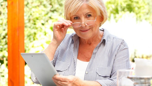 Portrait of retired woman sitting at the garden while using ebook reader. Senior female using digital tablet and relaxing in her beautiful garden at home.